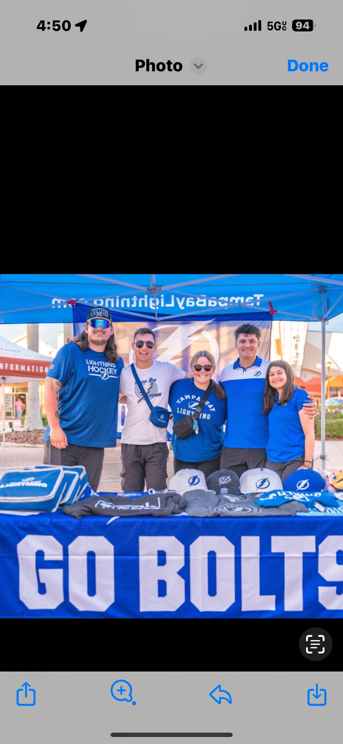 Tampa Bay Lightning team members at an outdoor promotional booth with a blue GO BOLTS table and branded merchandise display
