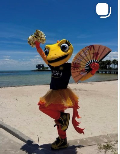 Solé mascot posing on a tropical beach with a gold pom-pom and decorative fan — Tampa Bay Sun FC mascot social content